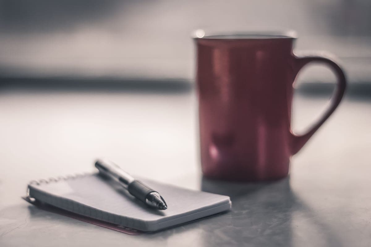 A quiet desk by a window in flat winter daylight, a notebook, a calculator and a mug.