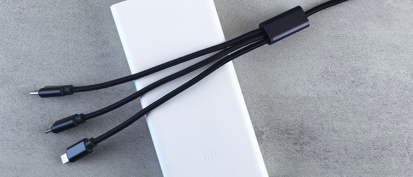 A white USB power bank with a charging cable laid on a plain pale surface.