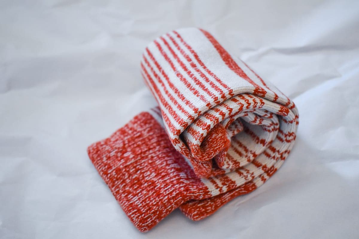A pair of thick socks and a small flat warmer packet on a pale wooden surface in soft light.