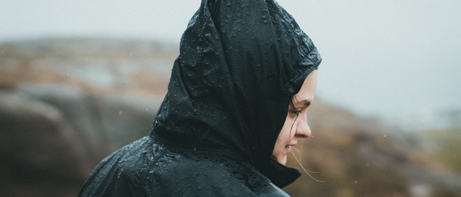 A person in a rain jacket outdoors in light rain under flat gray daylight.