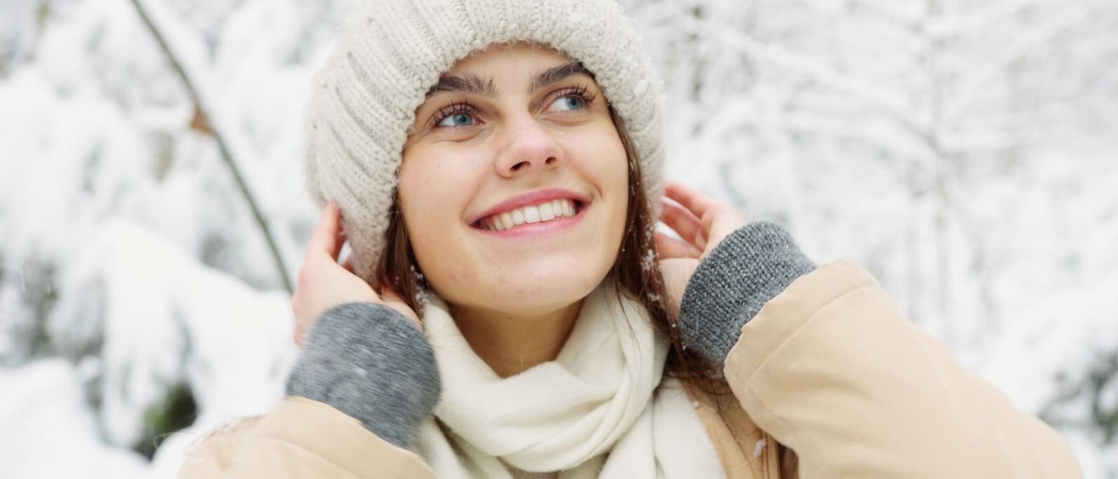 A person in a knitted hat and winter coat standing in snow under bright overcast daylight.