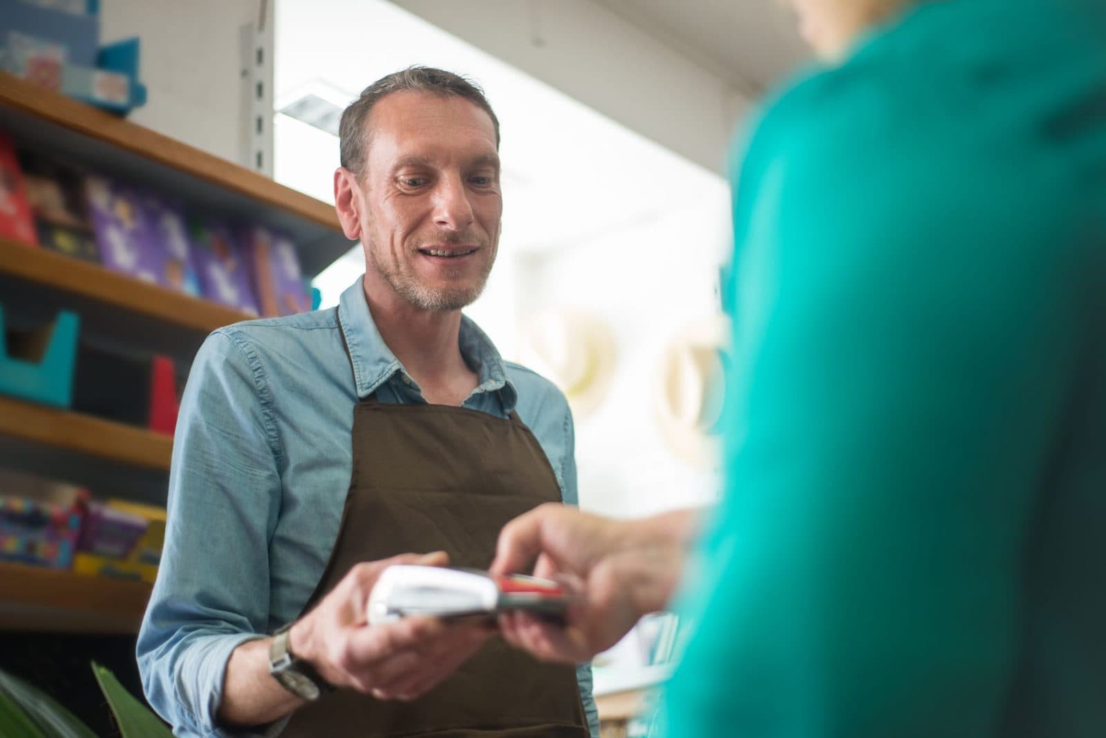 A male store clerk assisting a customer with a payment transaction in a retail shop setting.