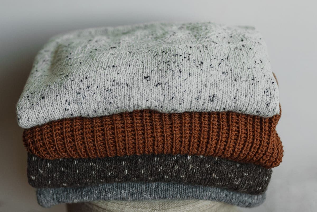 Folded base layers and a sweater stacked on a pale surface in soft daylight.