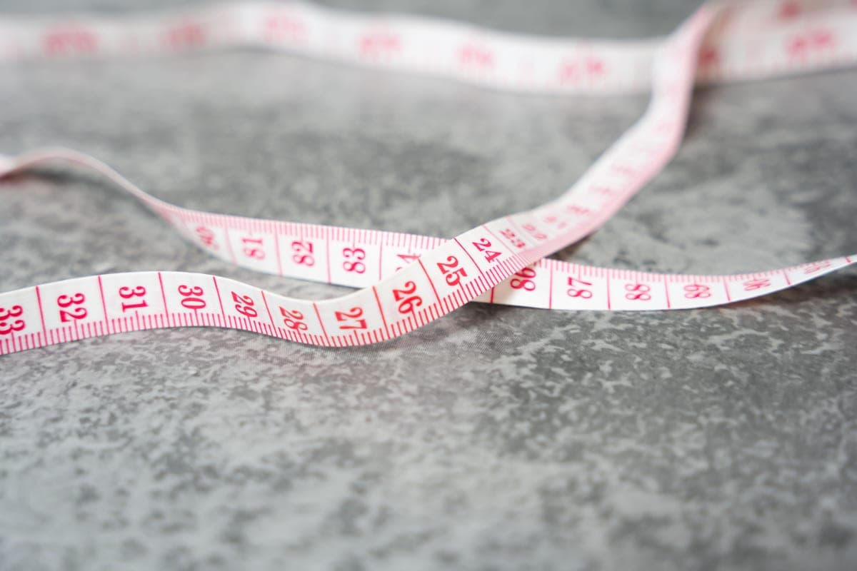 A tape measure and a folded jacket on a pale surface in soft, even daylight.
