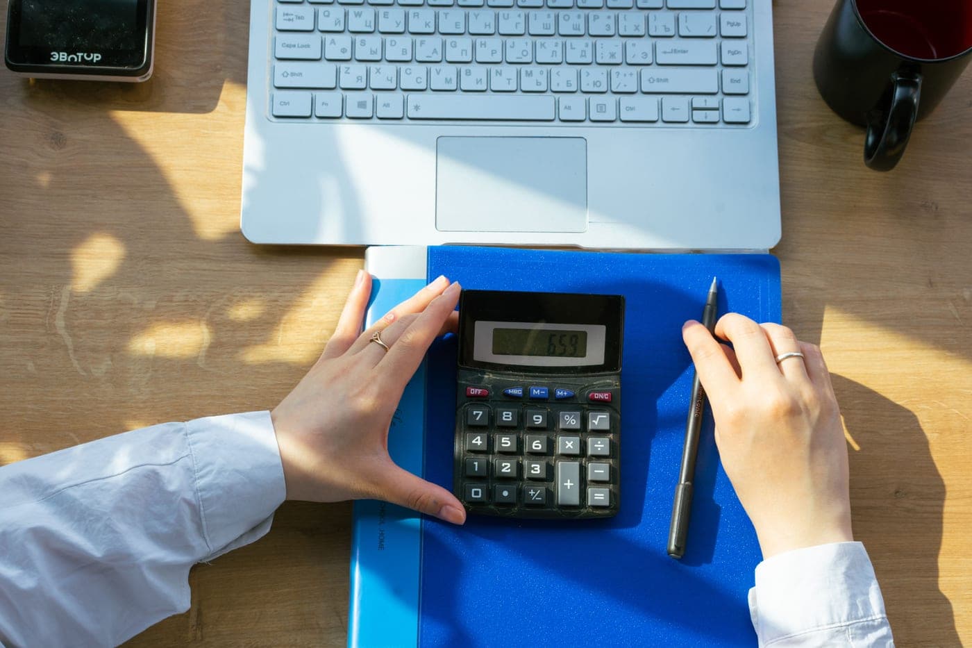 A notebook and a calculator on a pale desk in soft winter daylight, the working tools behind every figure on this site.