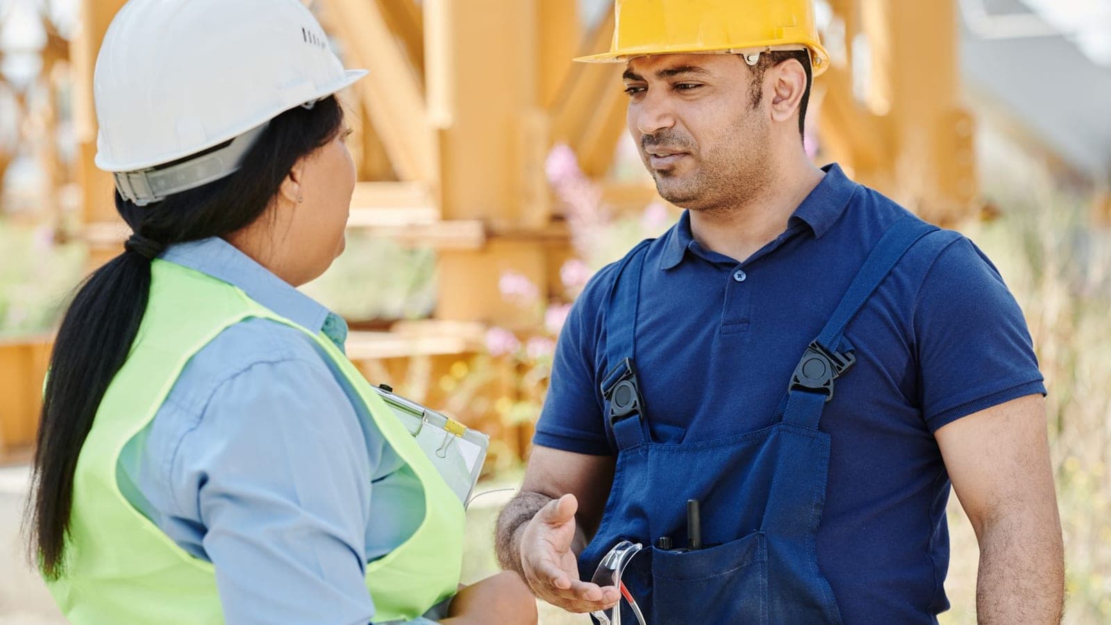 Male and female construction workers discussing safety on a sunny day outdoors.