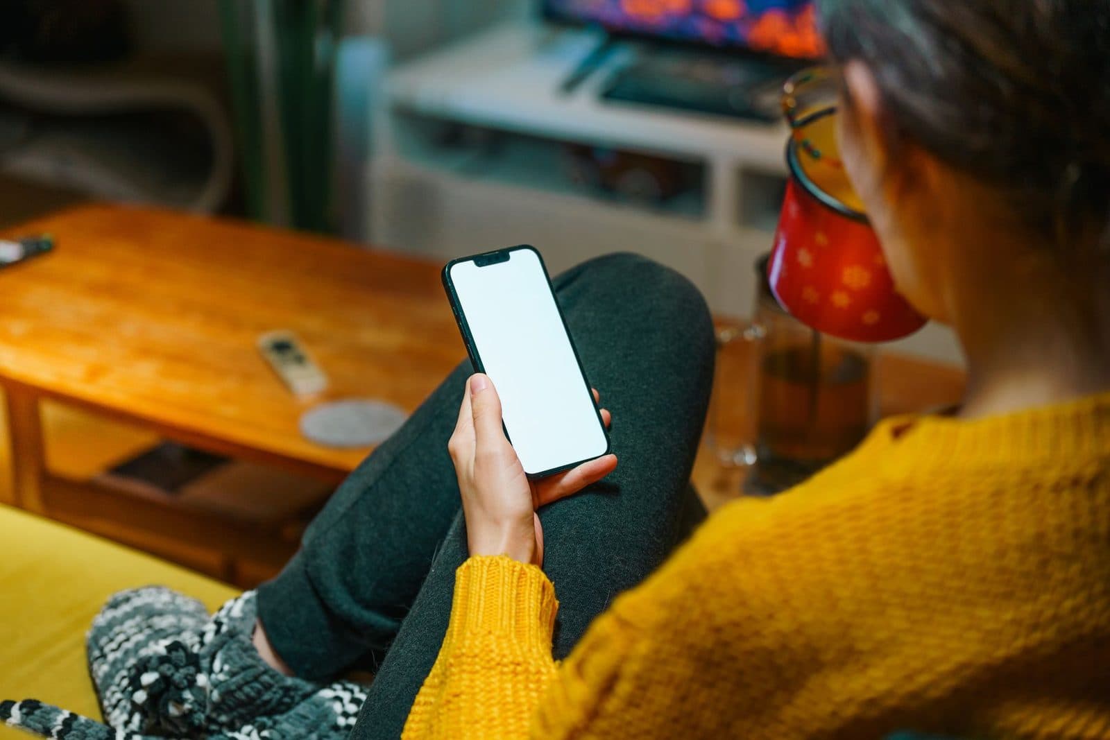 A person relaxing on a sofa with a smartphone, enjoying a warm winter evening indoors.