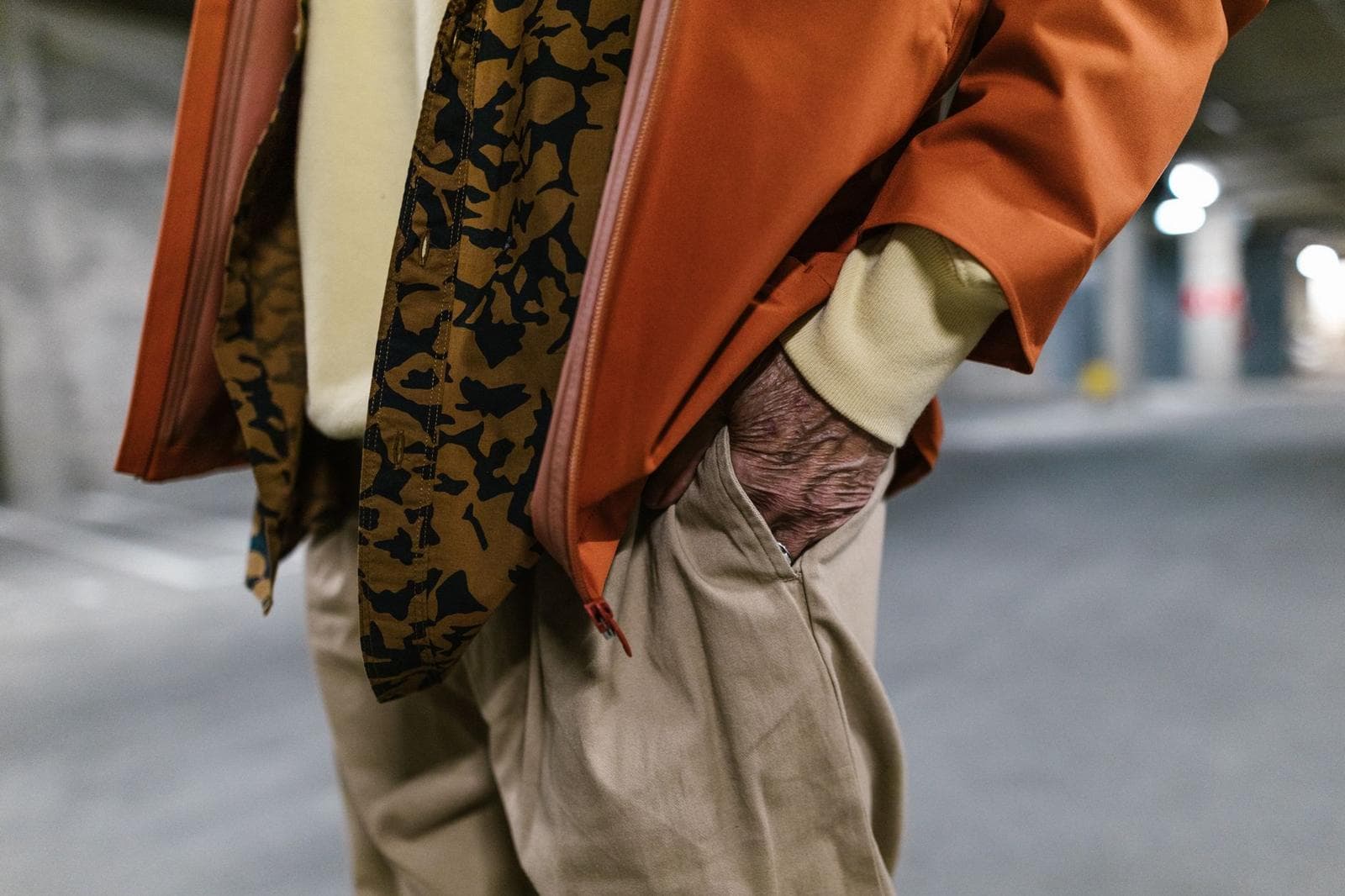 Close-up of a stylish senior adult wearing a rust jacket and khaki pants in an urban setting.