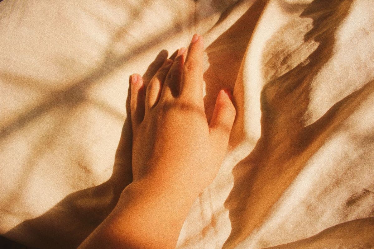 Hands resting on a pale blanket in soft indoor daylight, calm and unhurried.