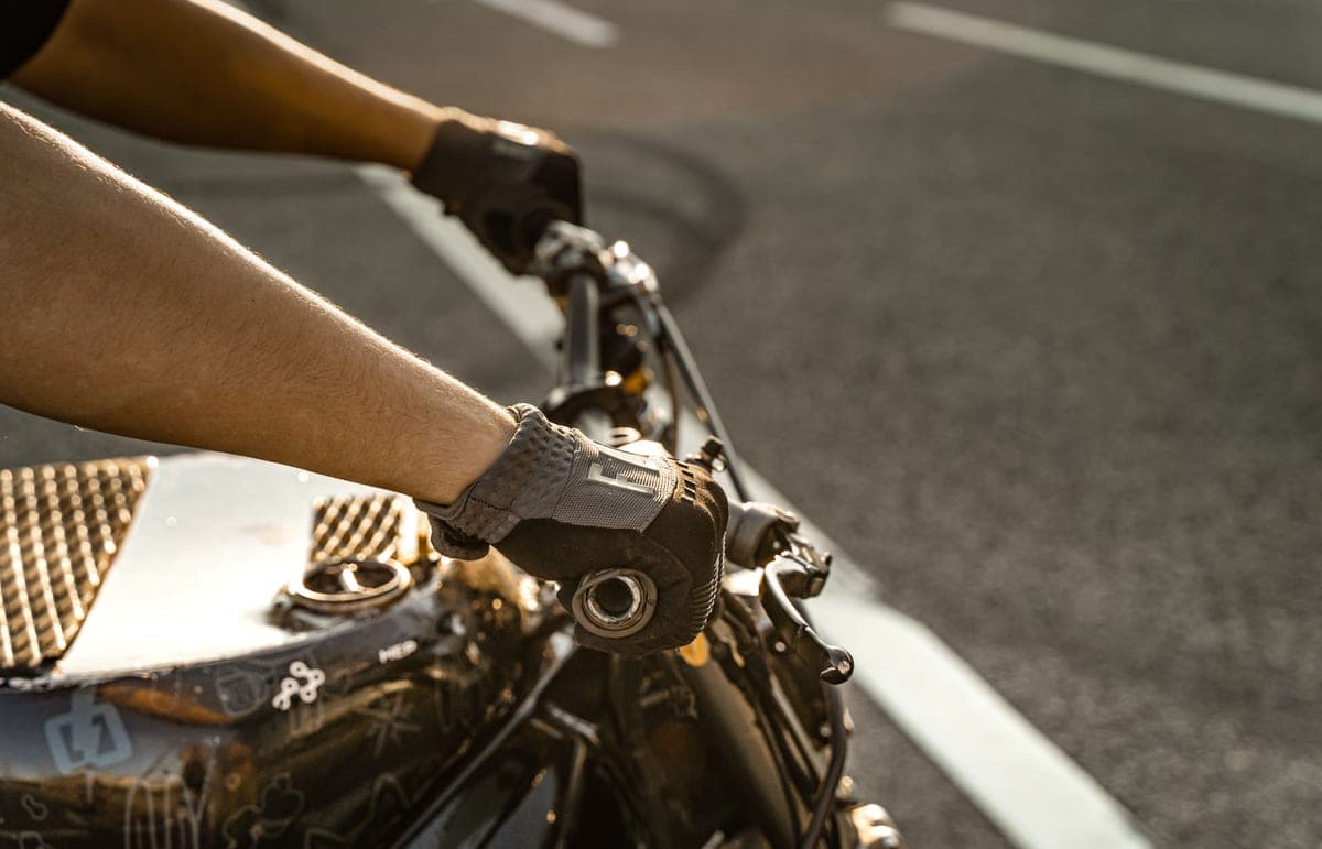Gloved hands on motorcycle handlebars under cold gray daylight.