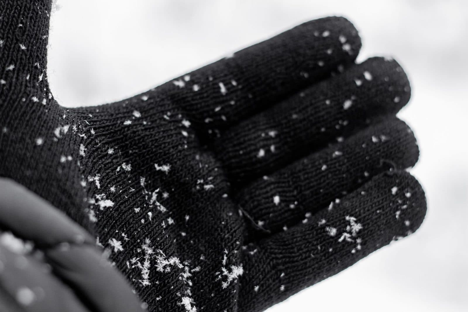 Black glove catching delicate snowflakes during a winter snowfall.