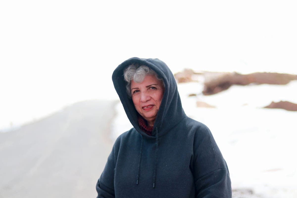 A person in a hooded sweatshirt outdoors on a cold overcast day, flat pale daylight.