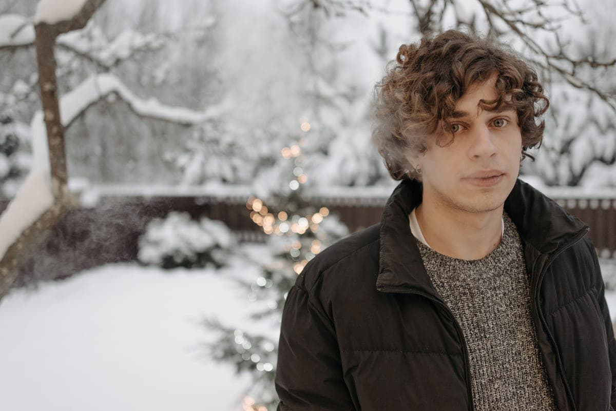 A man in a dark jacket standing on a frosted driveway in flat overcast winter light, breath visible.