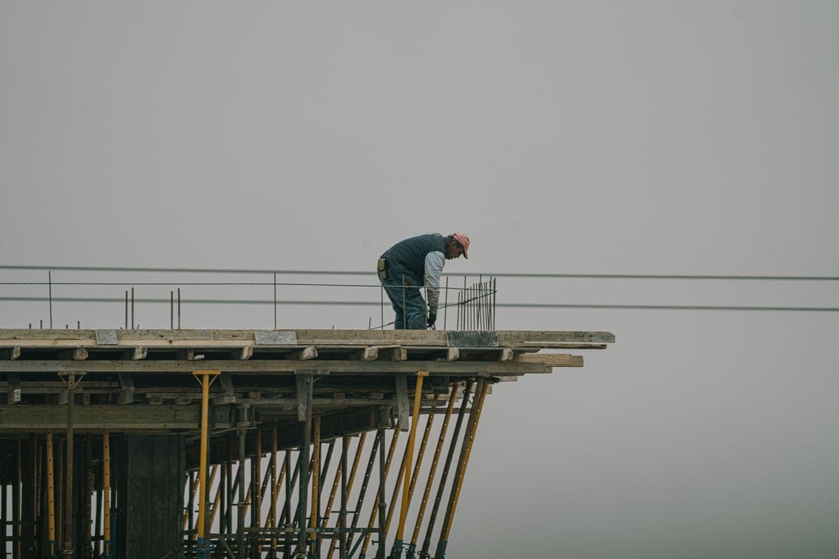 An early-morning construction site under pale overcast sky, scaffolding and frost on stacked timber.