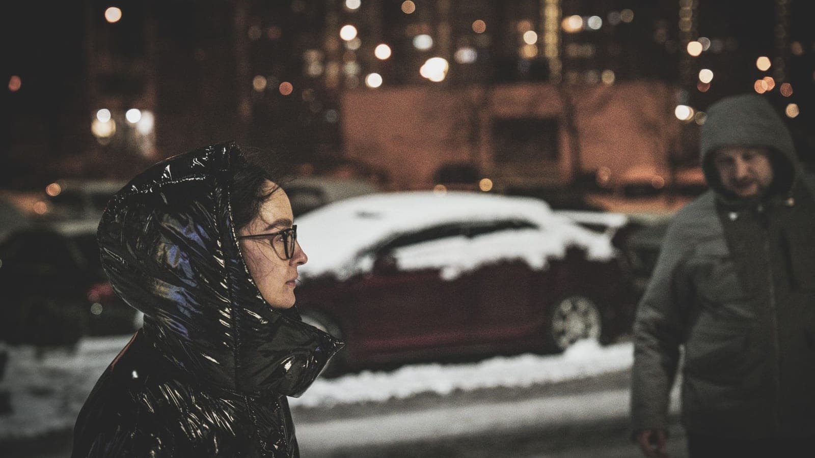 Two people walking in a snowy city street at night, urban winter atmosphere.