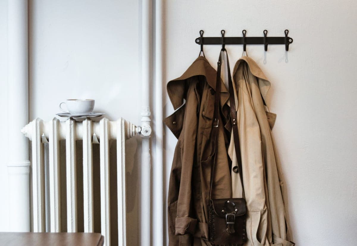 A row of winter jackets on a rail in soft, flat daylight against a pale wall.