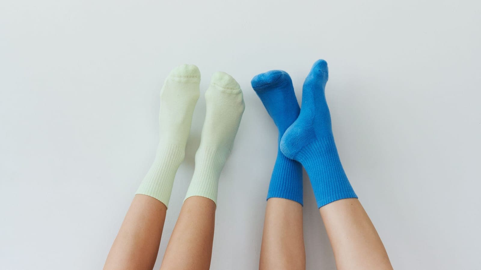 Two pairs of relaxed legs with pastel and vibrant socks on a clean white background.
