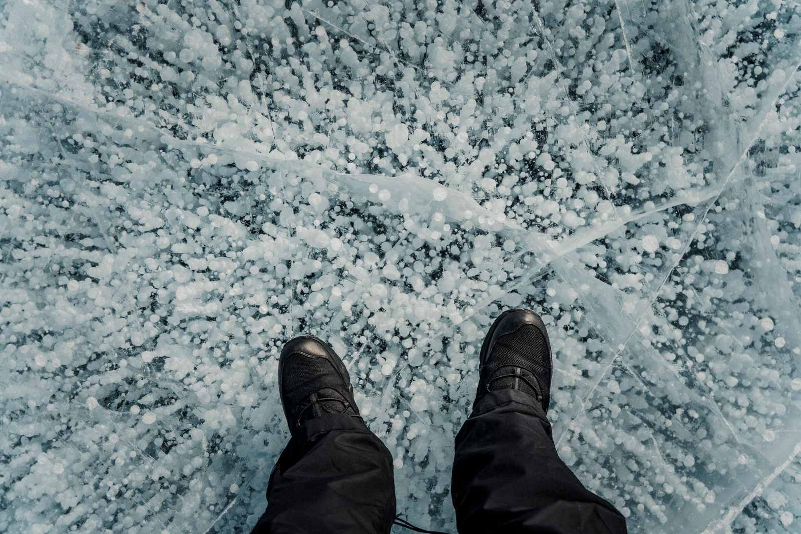 Top view of boots standing on uniquely patterned frozen ice with cracks.
