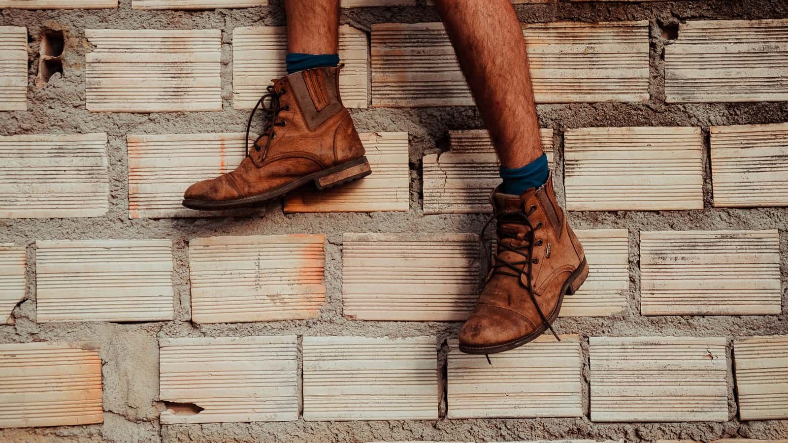 Brown leather boots on a textured brick wall background, casual fashion display.