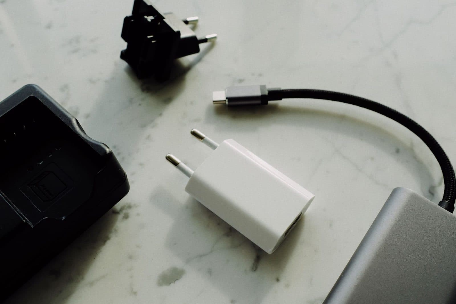 Set of various modern charging unit with adapter and small external battery pack with short cable placed on white marble table.