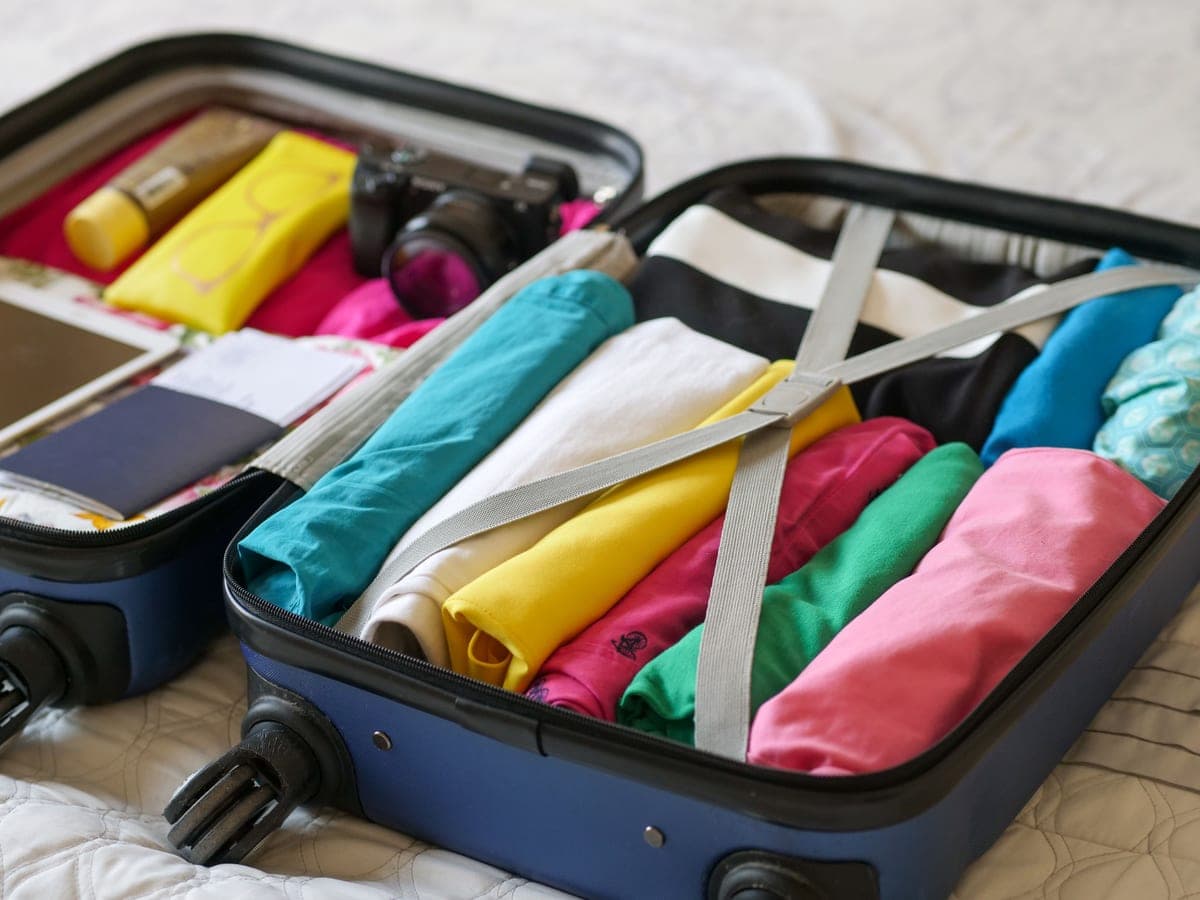 A packed carry-on bag open on a bed with a folded jacket and a small battery pack, soft daylight.