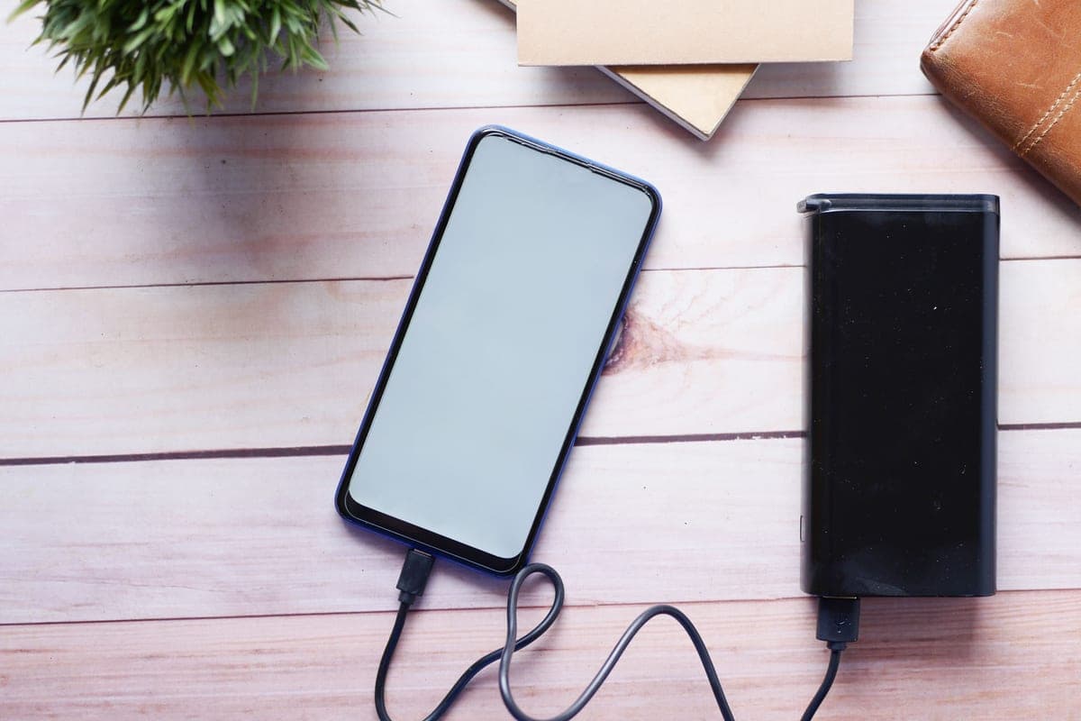 A charging cable and small battery pack on a pale desk beside a folded jacket, soft daylight.