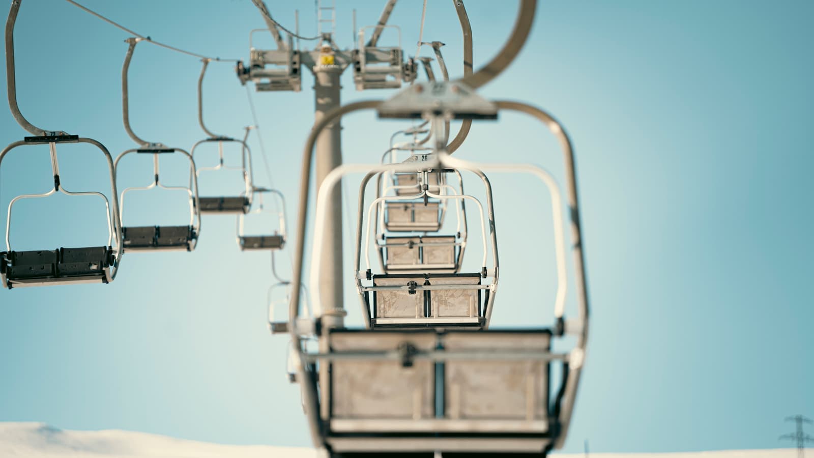 A row of empty ski lift chairs captured from below with a clear sky in the background.