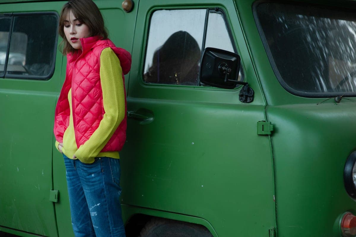 A woman in a light quilted vest over a knit sweater, standing outdoors in flat pale winter daylight.