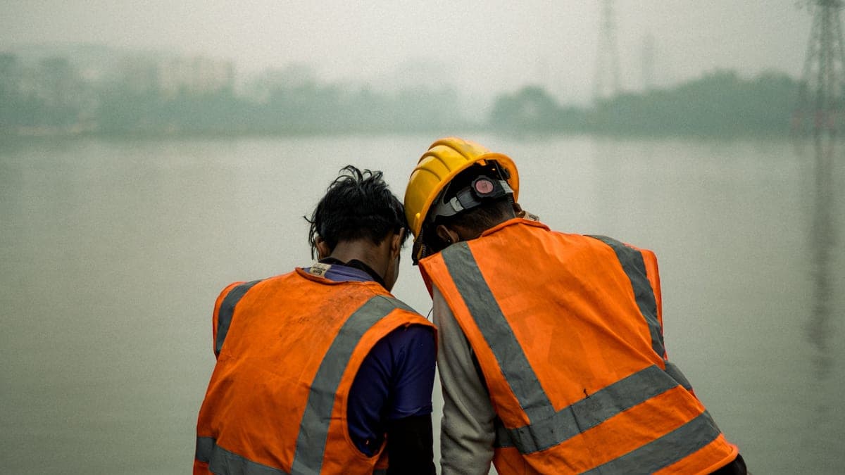 A worker in a vest on a cold site under pale overcast morning light.