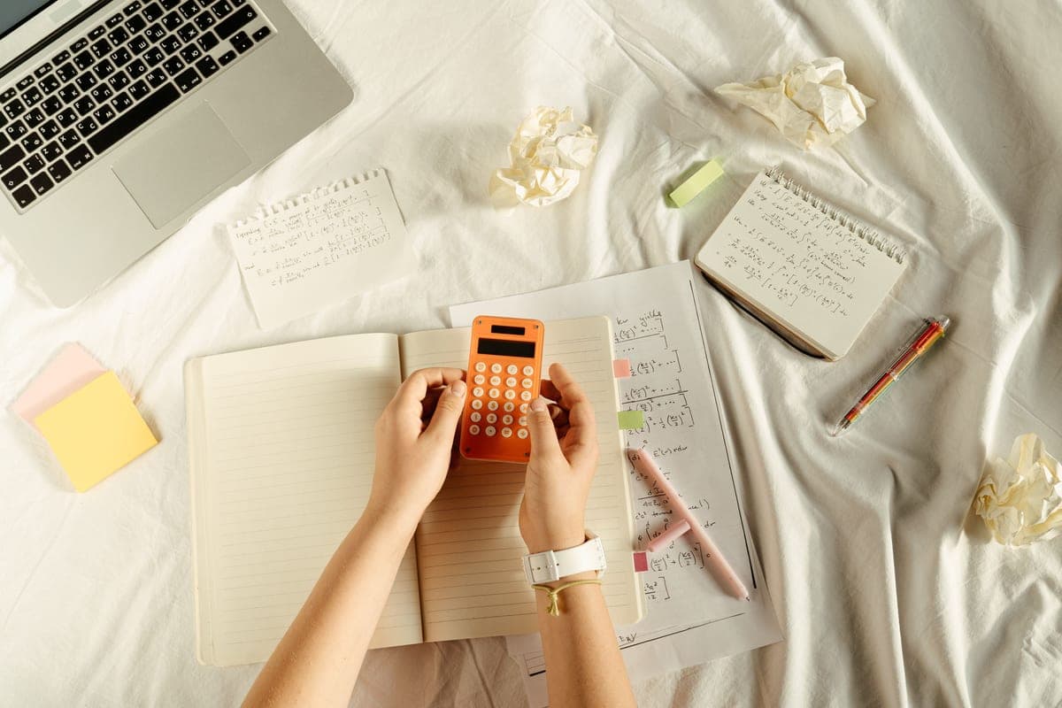 A notebook page of handwritten arithmetic beside a small battery pack in soft daylight.